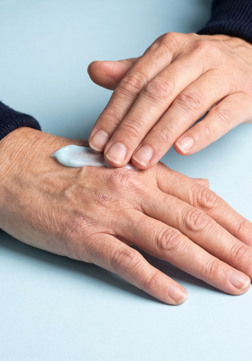A dab of pale blue balm being pressed into the back of a hand