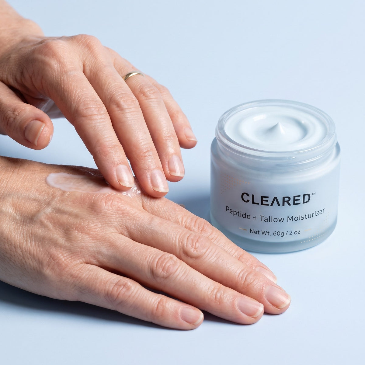 Hands pressing in pale blue balm next to a jar of CLEARED
