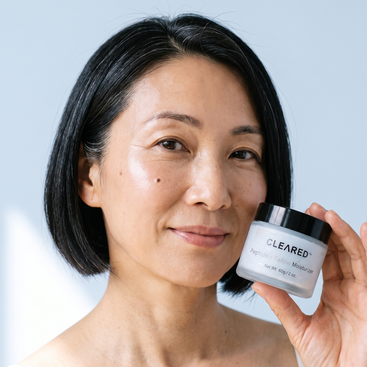 A Japanese woman in her fifties with soft, glowing skin holding a jar of CLEARED balm